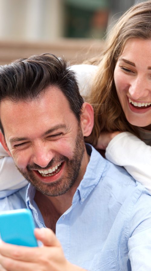 Close up portrait of laughing couple sitting together in embrace with mobile phone