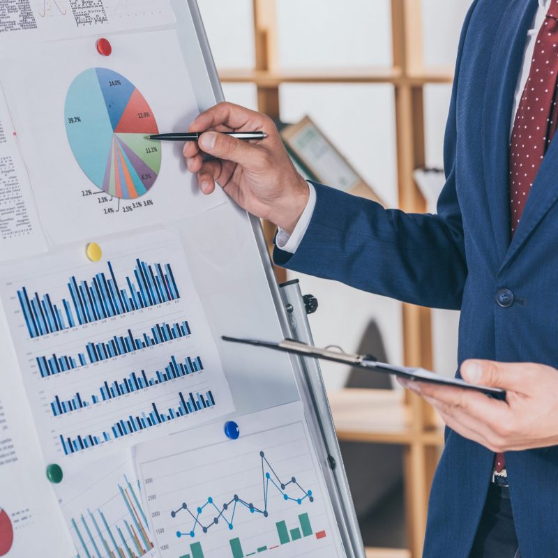 cropped view of businessman in formal wear analyzing infographics on flipchart