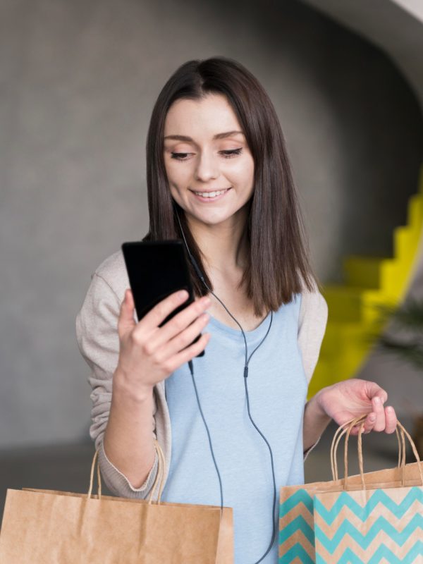 front-view-smiley-woman-holding-smartphone-paper-bags