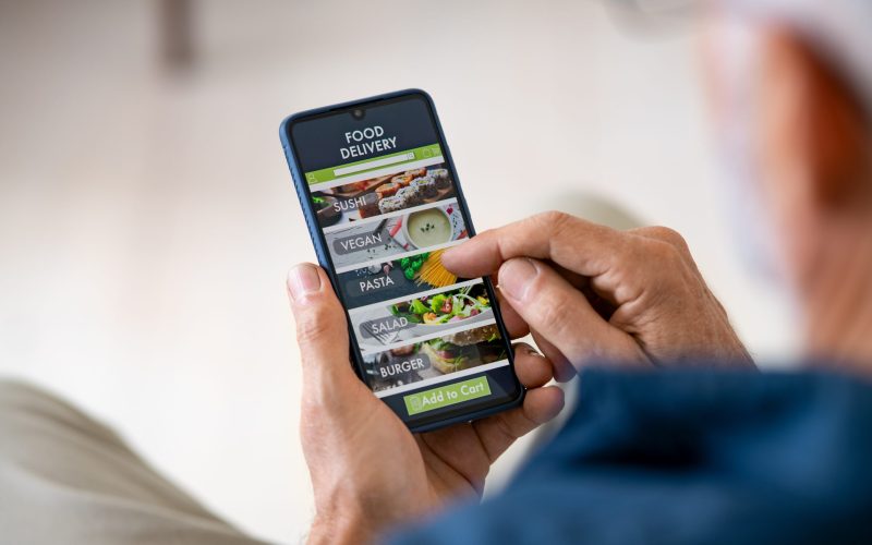 Top view of man hands holding smartphone while order food delivery at home. Back view of mature man using food delivery app with mobile phone to order lunch.